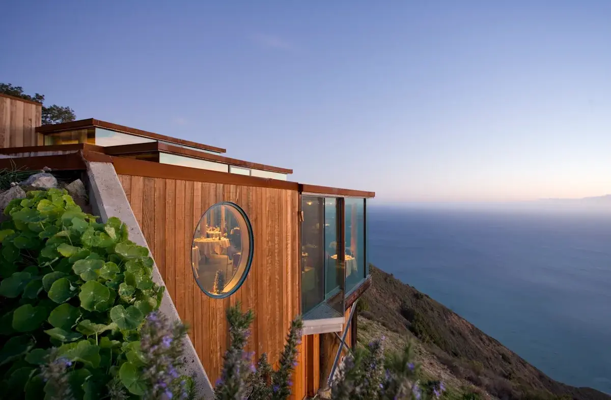 A wooden building perched on a cliffside overlooks the ocean