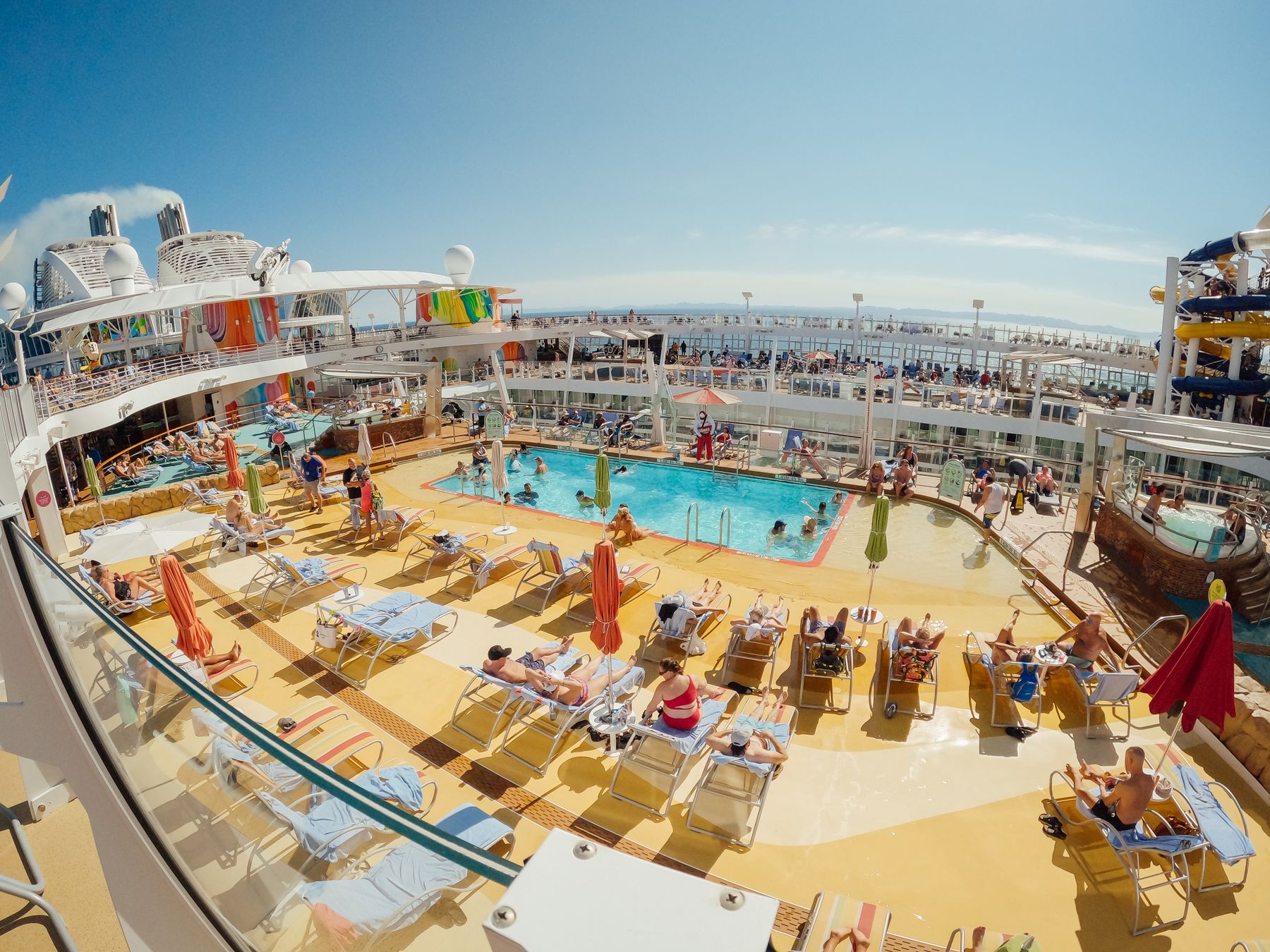 Sunbathers and swimmers around the main pool deck of a large contemporary cruise ship