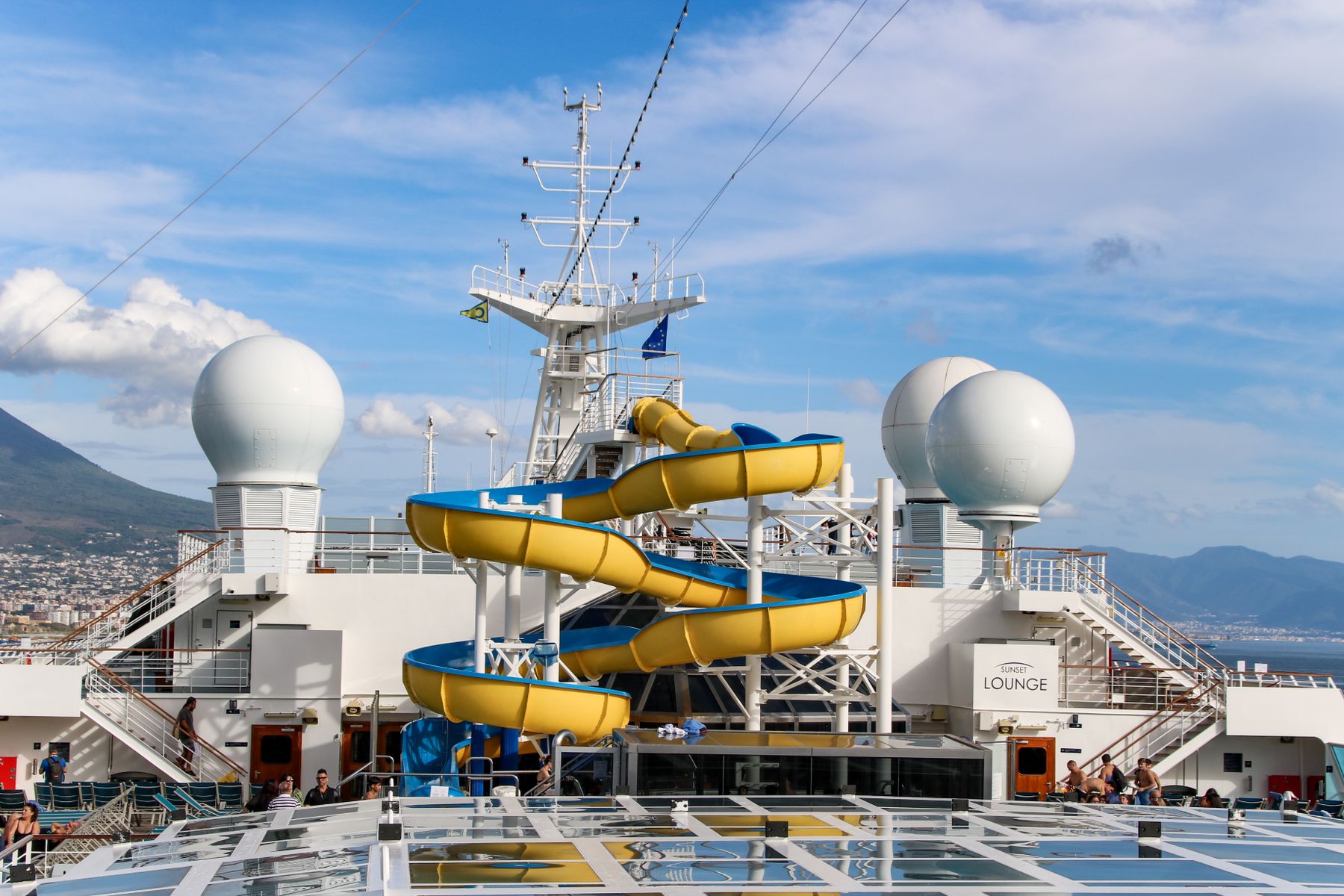 Cruise ship top deck with a yellow and blue waterslide under a bright sky, a favorite feature on family cruises