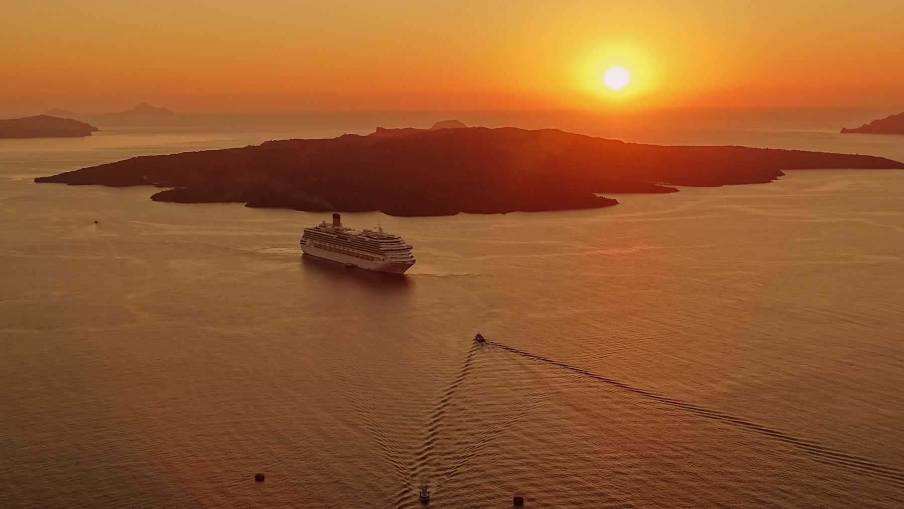 Cruise ship anchored in the Santorini caldera at sunset with the volcanic island silhouetted on the horizon
